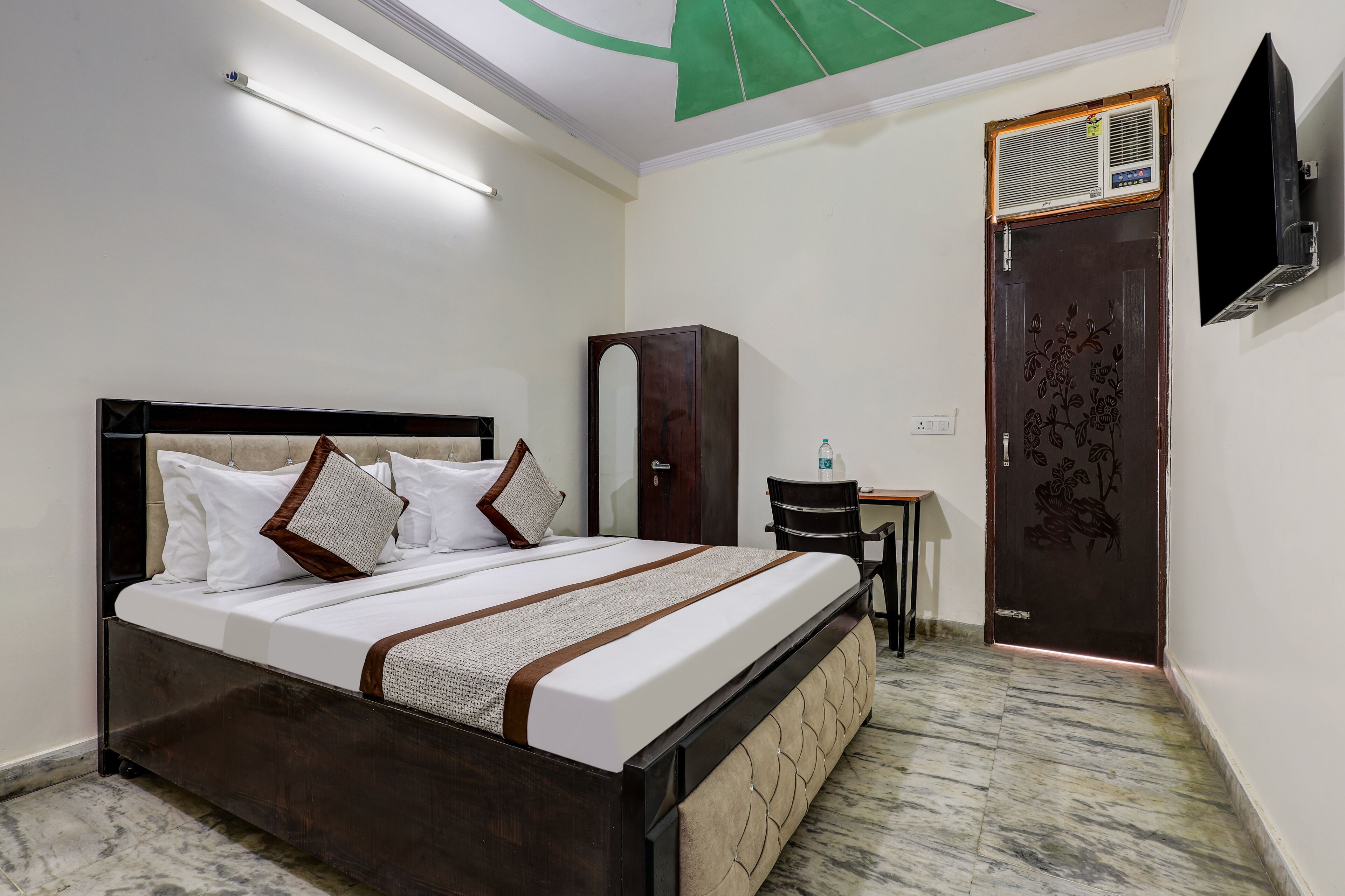A neatly made bed with a headboard, a wardrobe, a desk with a chair, and a door with a decorative panel.