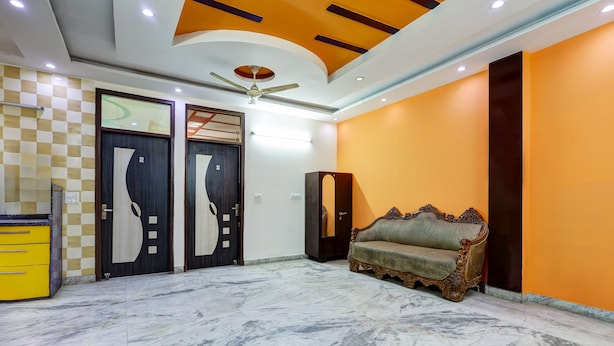 A spacious room with a marble floor, a ceiling fan, and a sofa against an orange wall. - Hotel Sunshine By The Premium Villa (New Delhi)