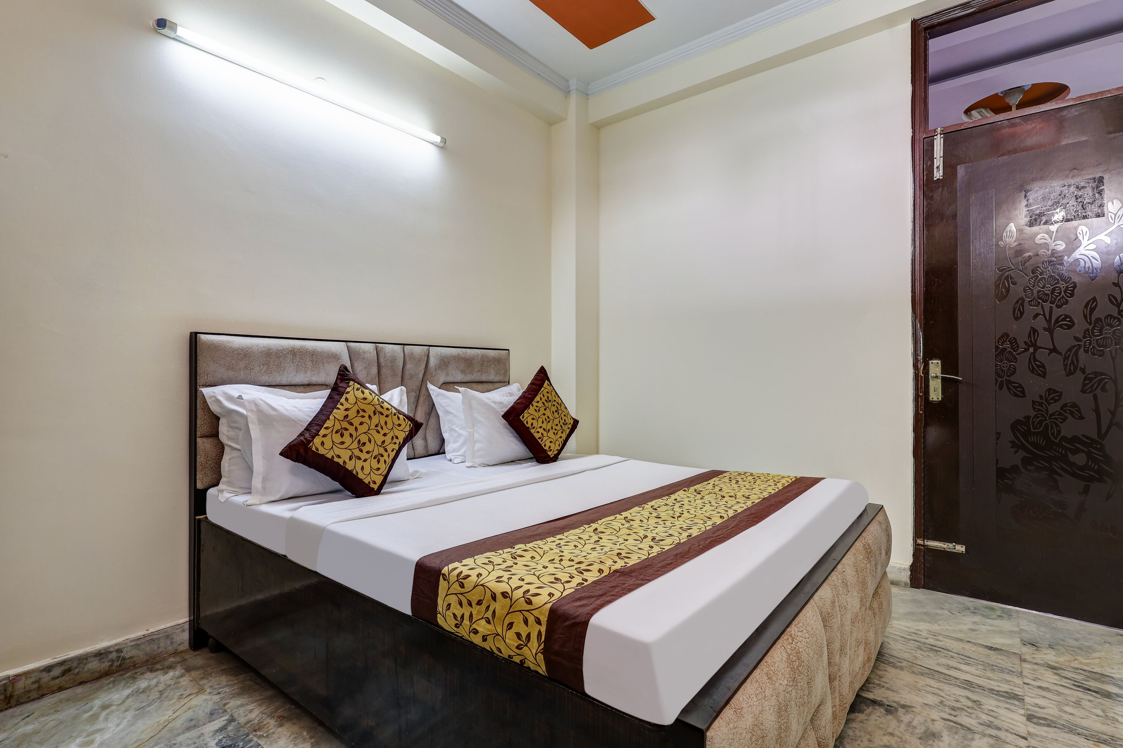 A neatly made bed with a patterned bedspread and pillows, a bedside table, and a door with a floral design.