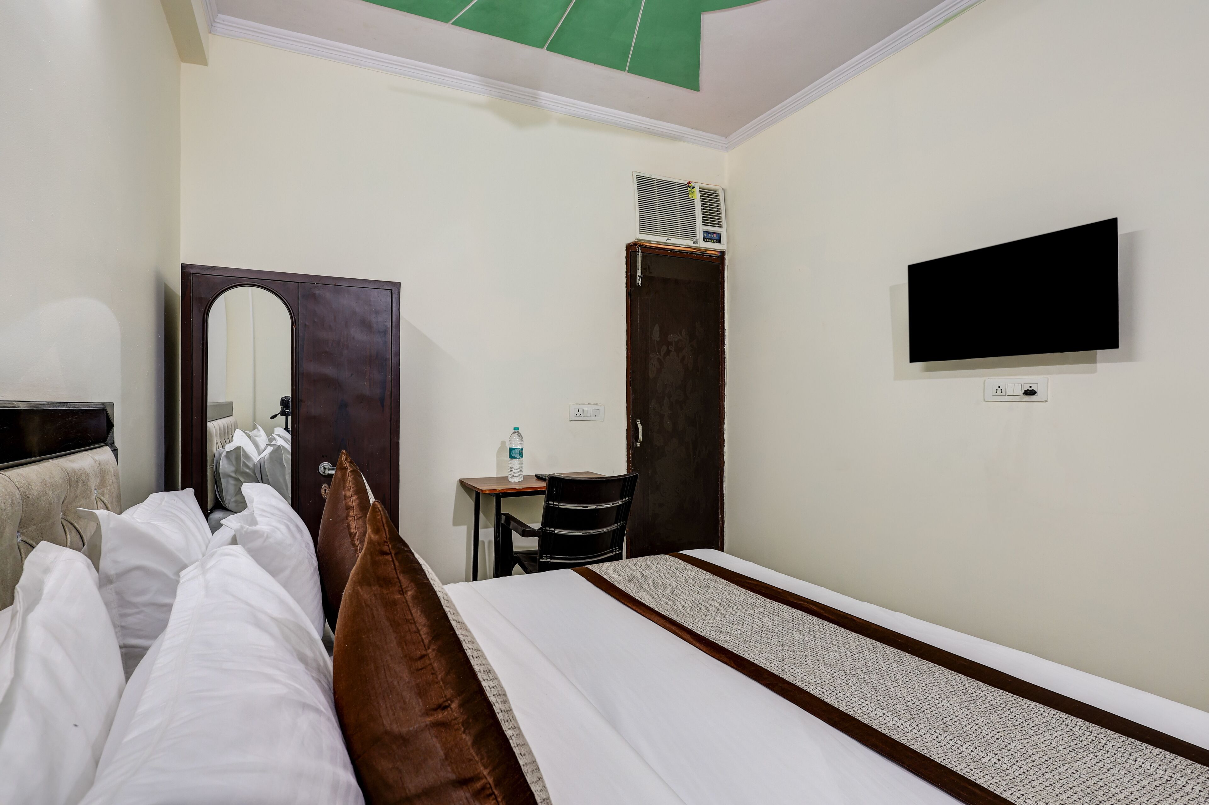 Une chambre d’hôtel équipée d’un lit, d’un bureau, d’une chaise, d’un miroir, d’une télévision et d’un appareil de climatisation.