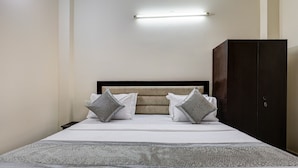A neatly made bed with a headboard, two pillows, and a bedside table with a lamp. - Hotel Sunshine By The Premium Villa (New Delhi)