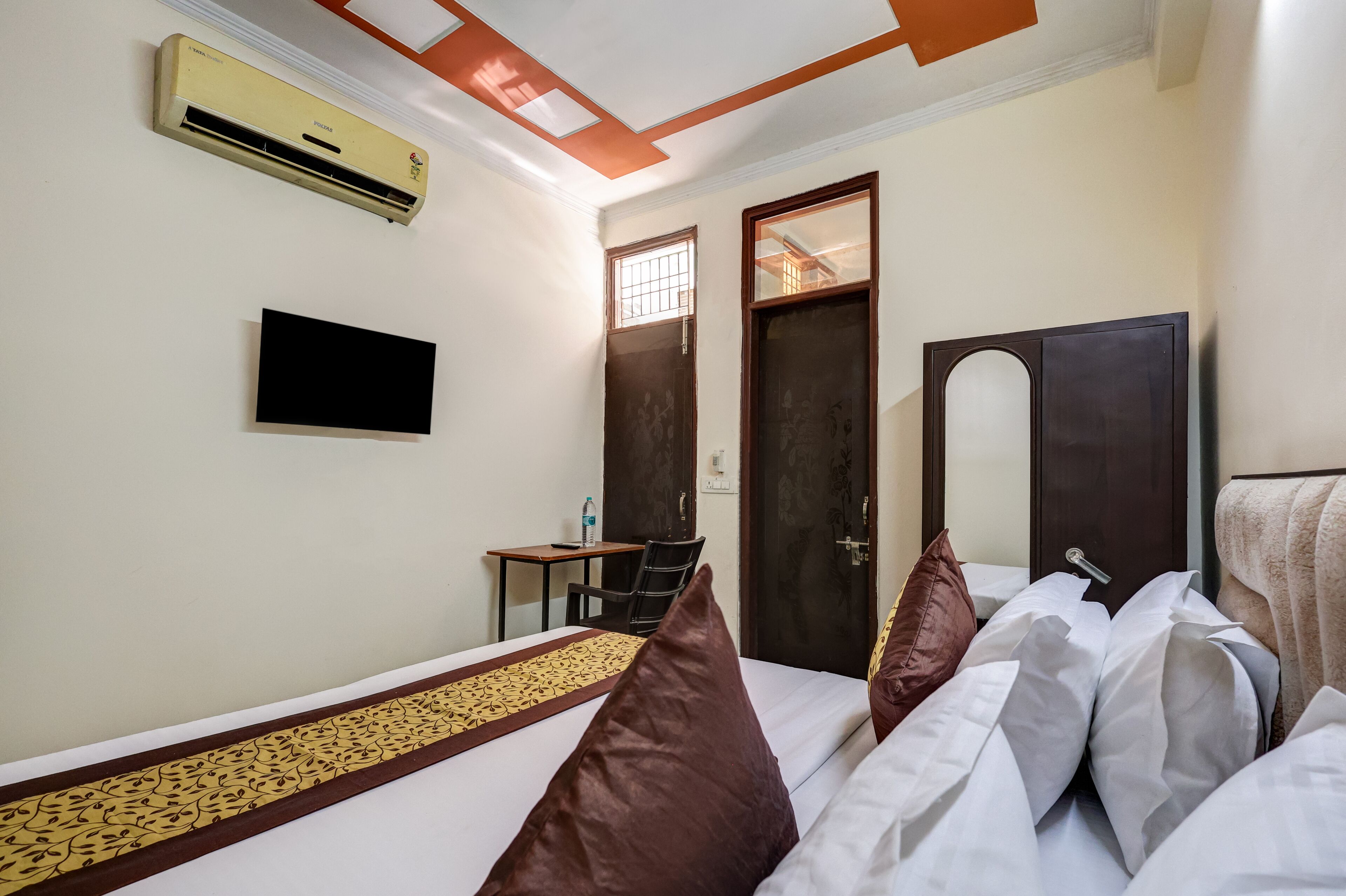 Een hotelkamer met een bed, een bureau, een stoel, een airconditioner en een televisie.