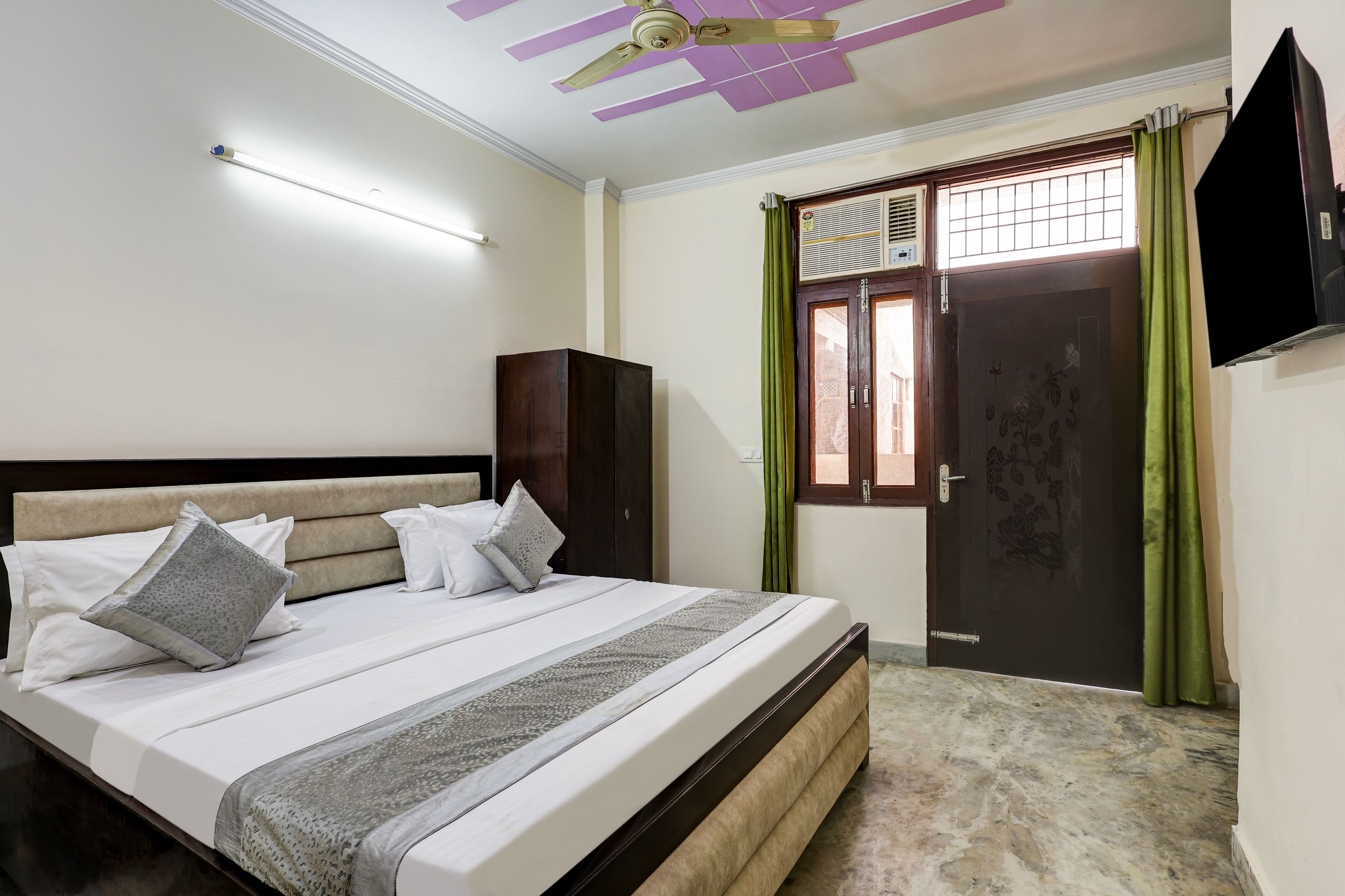 A bedroom with a bed, a wardrobe, a ceiling fan, a TV, and a window with curtains.