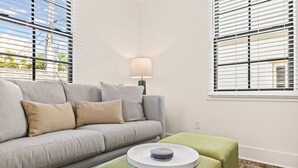 A modern living room with a grey sofa, a green ottoman, and a lamp. - Pet-friendly Renovated Apt Steps to Forsyth, Coffee Shops by Lucky Savannah (Savannah)