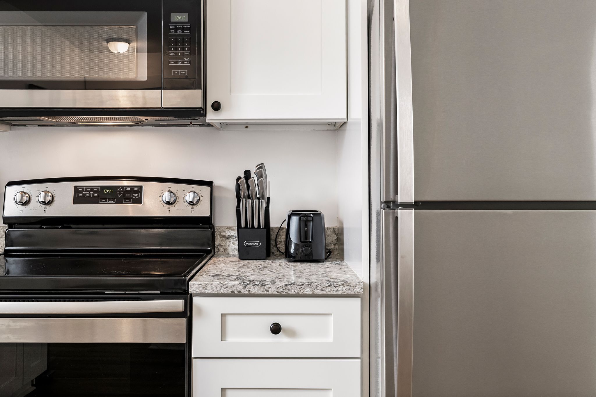 A kitchen with a stainless steel stove, microwave, and refrigerator, along with a toaster and knives on the counter.