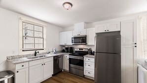 A modern kitchen with white cabinets, stainless steel appliances, and a wooden floor. - Pet-friendly Renovated Apt Steps to Forsyth, Coffee Shops by Lucky Savannah (Savannah)