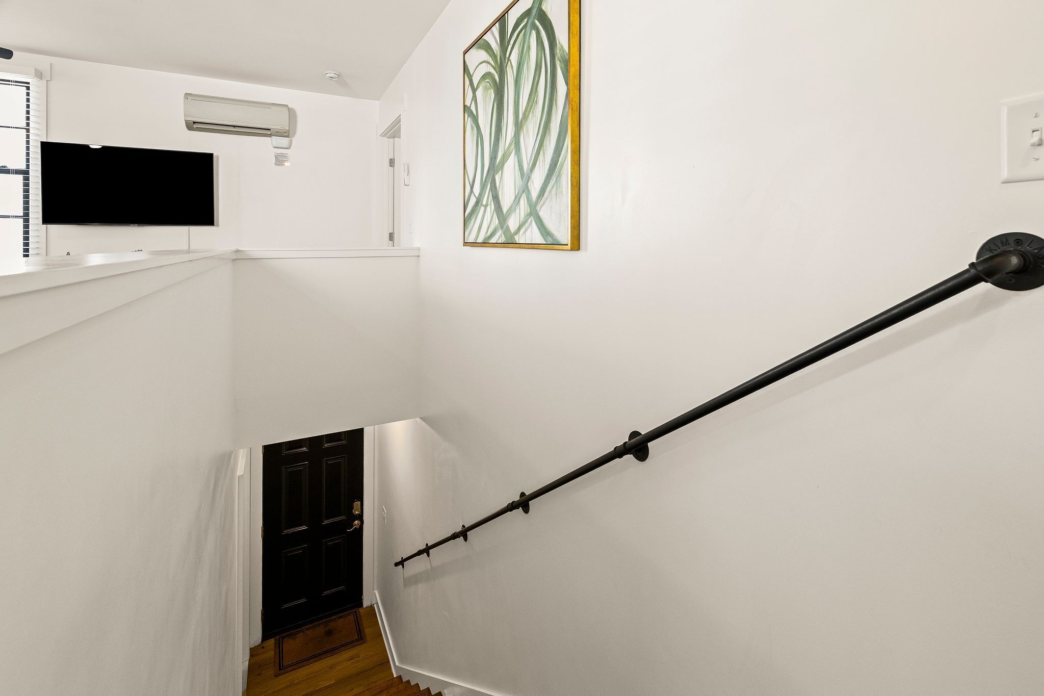A staircase with a handrail, a wall-mounted air conditioner, and a painting.