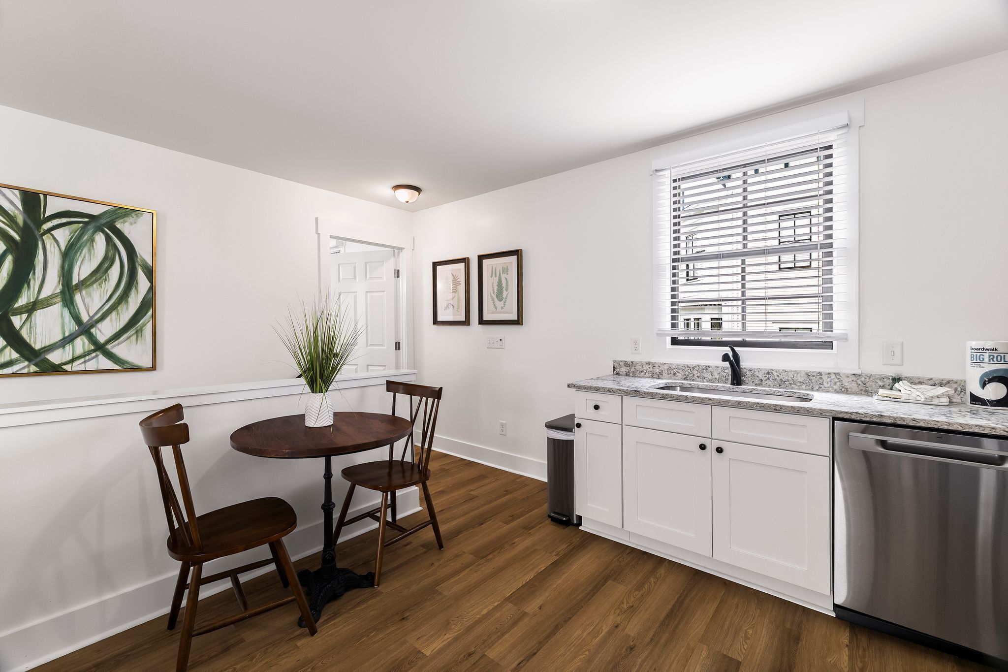 A modern kitchen with white cabinetry, a stainless steel dishwasher, and a window with blinds.