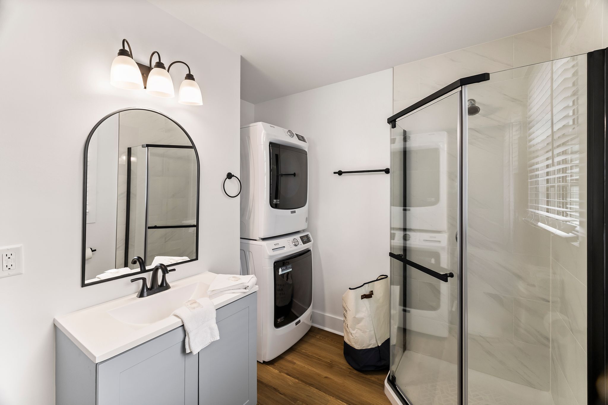 Een moderne badkamer met een wastafel, spiegel, ingebouwde wasmachine en douchecabine van glas.