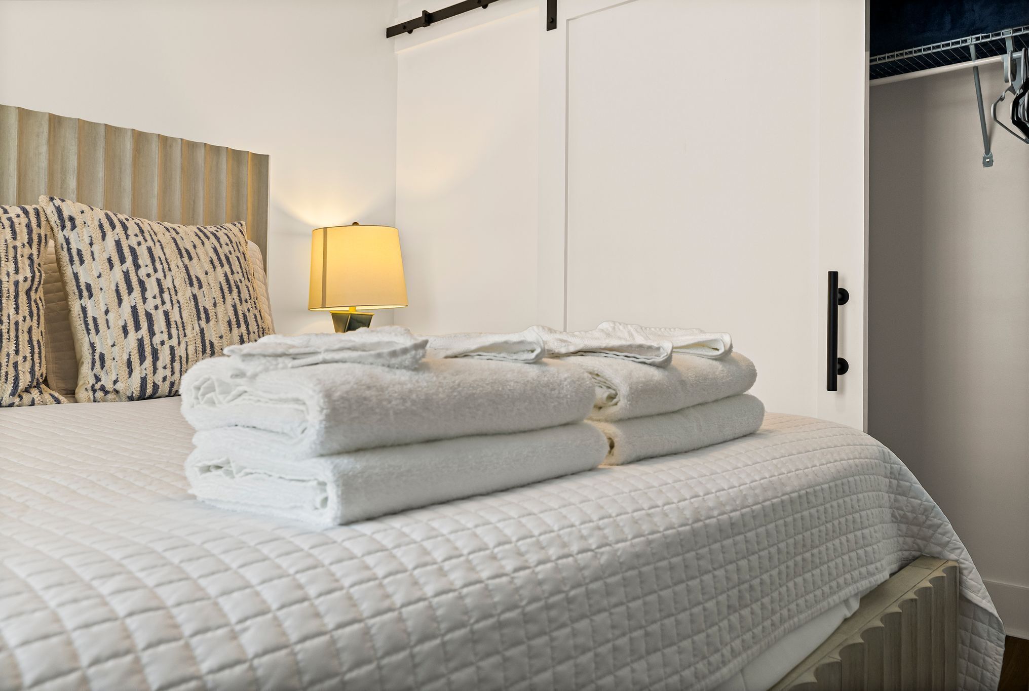 A neatly made bed with folded towels, a bedside lamp, and a wardrobe with a handle.