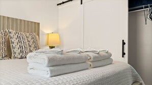 A neatly made bed with folded towels, a bedside lamp, and a wardrobe with a handle. - Pet-friendly Renovated Apt Steps to Forsyth, Coffee Shops by Lucky Savannah (Savannah)