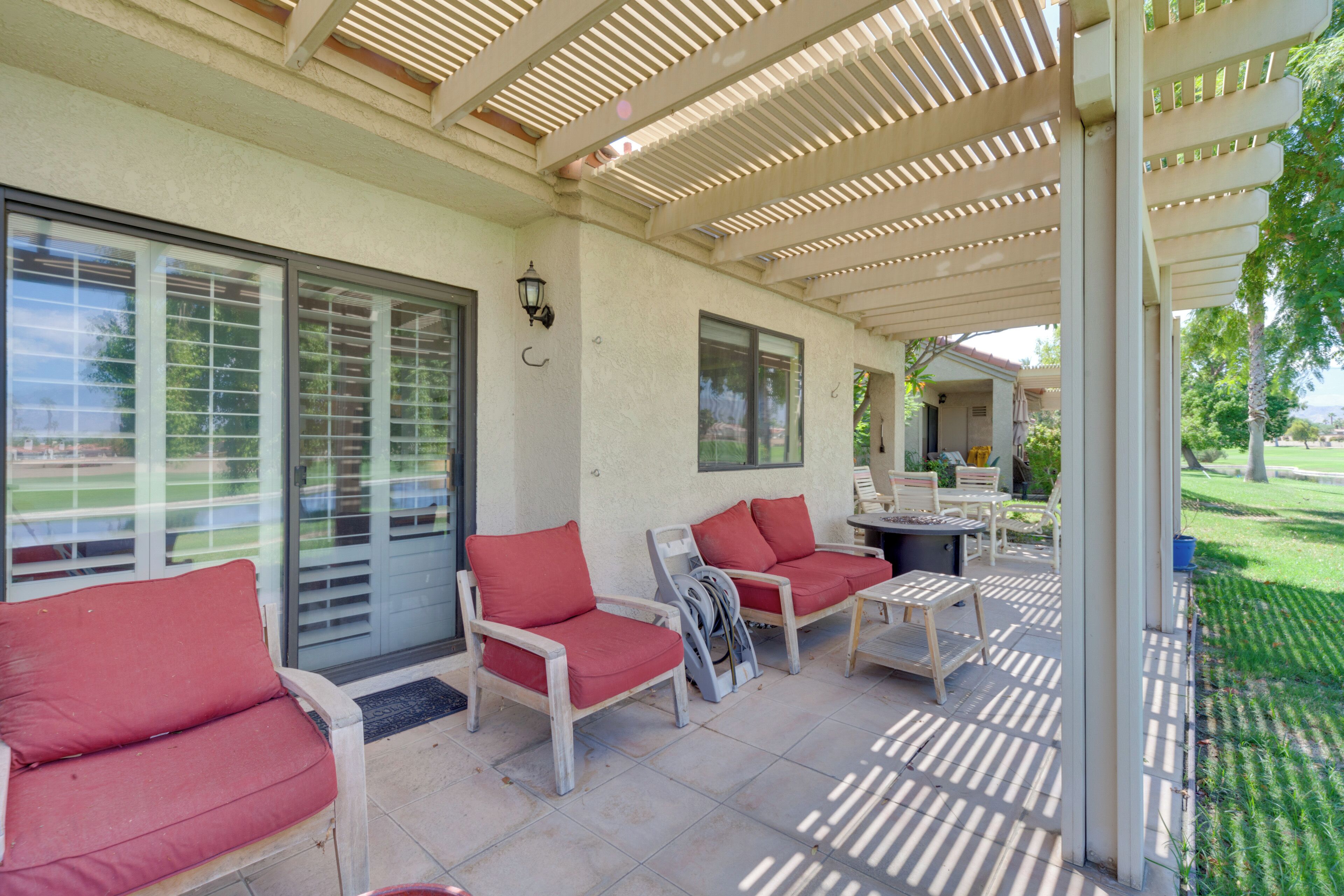 A covered patio area with seating and a table, featuring a pergola overhead.