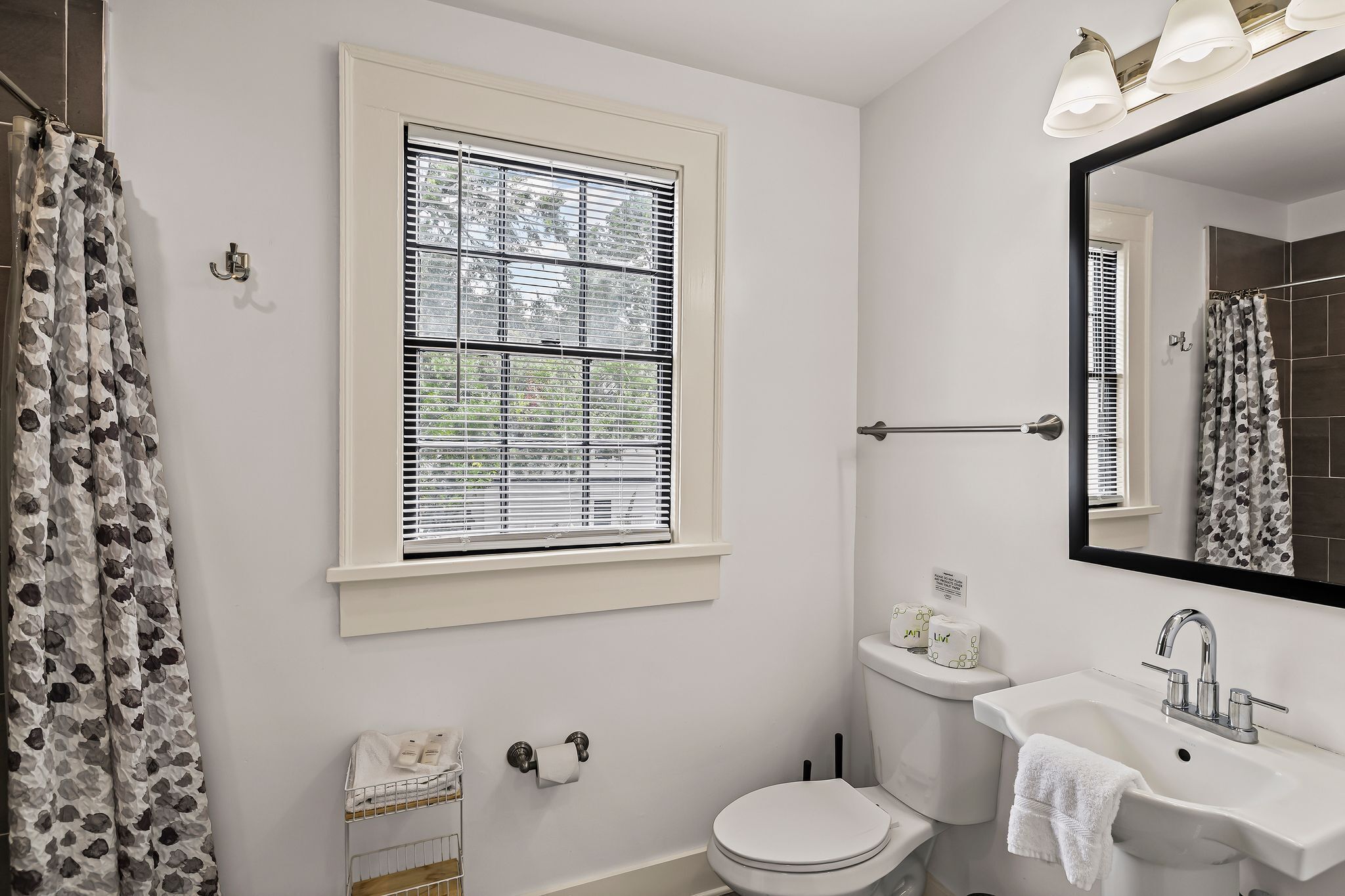 Une salle de bain avec des toilettes, un lavabo et une fenêtre équipée de stores.