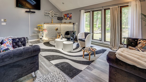 A modern living room with a fireplace, comfortable seating, and large windows. - Poconos Family Home w/ Game Room + Community Perks (East Stroudsburg)