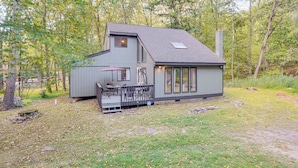A two-story cabin with a deck and a chimney, surrounded by trees. - Poconos Family Home w/ Game Room + Community Perks (East Stroudsburg)