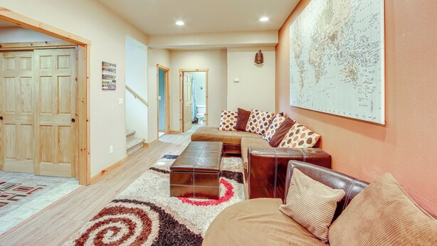 A spacious living room with a large sectional sofa, a coffee table, and a world map on the wall. - < 2 Mi to Granby Ranch: Home w/ Hot Tub & Decks! (Granby)