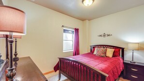 A bedroom with a wooden bed, a nightstand, a lamp, a window with curtains, and a wall decoration. - < 2 Mi to Granby Ranch: Home w/ Hot Tub & Decks! (Granby)