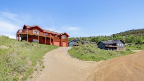 A rural road leading to a large wooden house with a balcony, surrounded by greenery and other houses. - < 2 Mi to Granby Ranch: Home w/ Hot Tub & Decks! (Granby)