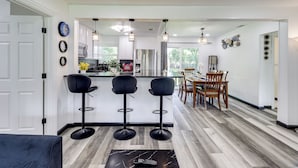 A modern kitchen with a central island, bar stools, and a dining area with wooden chairs.