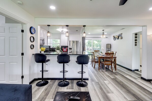 A modern kitchen with a central island, bar stools, and a dining area with wooden chairs.