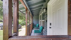 A covered porch with wooden railings, a white door, and two green chairs.