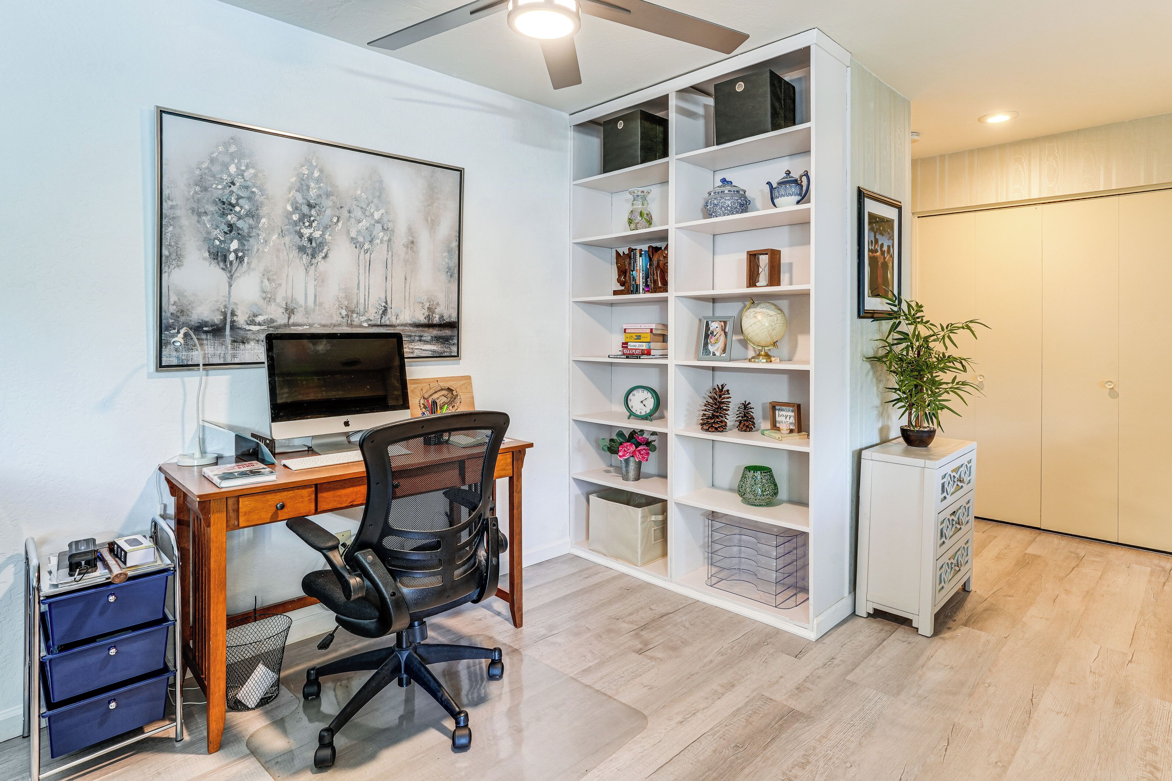 A home office with a desk, computer, chair, bookshelf, and decorative items.