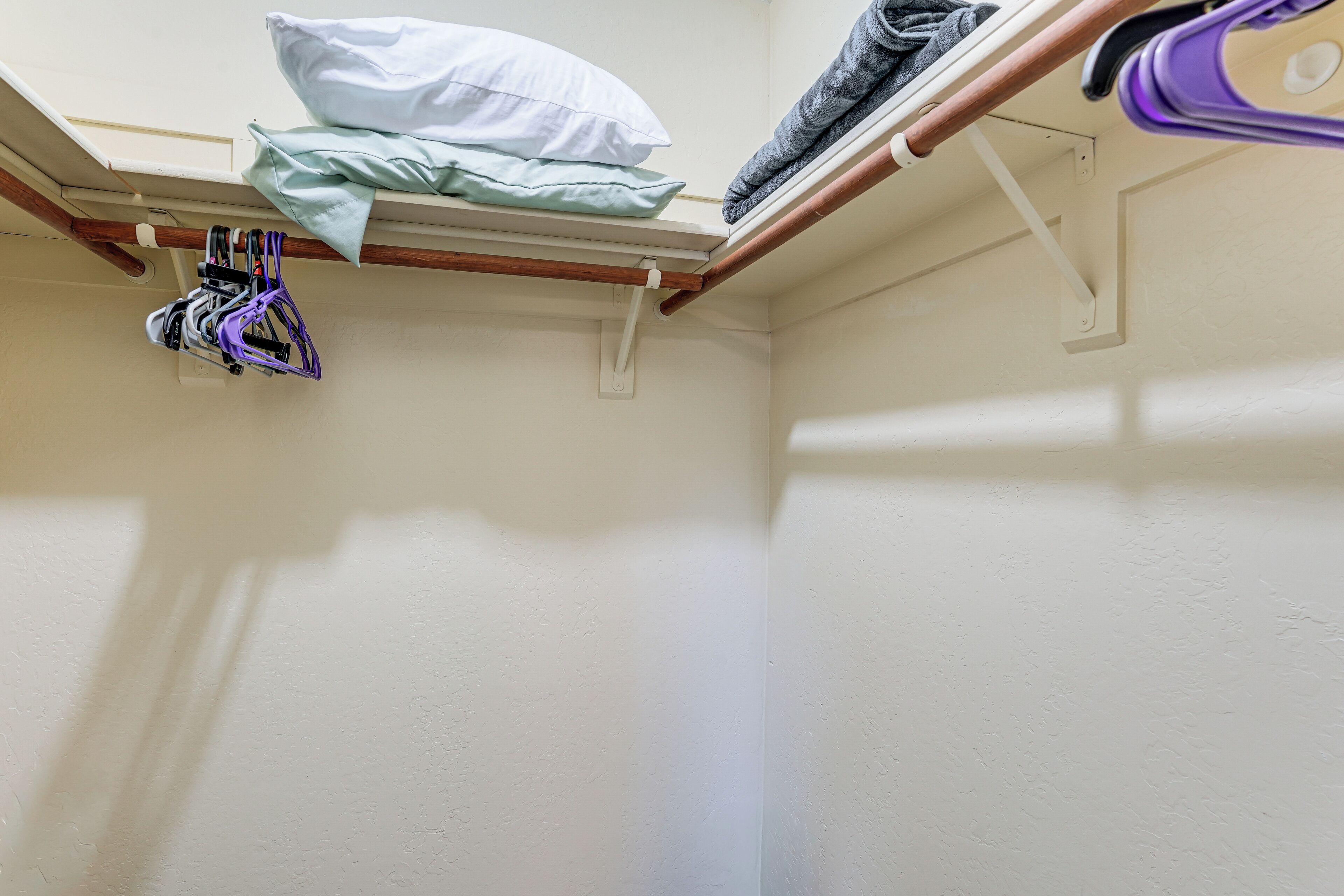 A corner of a room with a white wall, a wooden beam, and a shelf with folded clothes and a purple item.