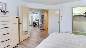 Ein Schlafzimmer mit Bett, Schminktisch und Kleiderschrank. Eine Tür führt in einen anderen Raum mit Schreibtisch und Stuhl.