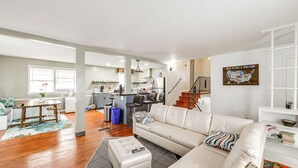 Ein modernes Wohnzimmer mit einer Couch, einem Hocker und einem Essbereich mit Tisch und Stühlen.