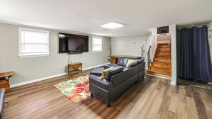 Ein Wohnzimmer mit einer Couch, einem Flachbildfernseher, einer Holztreppe und einem kleinen Tisch.
