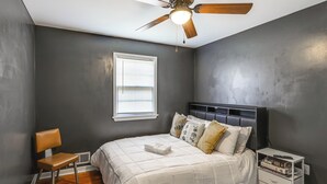 Ein Schlafzimmer mit Bett, Stuhl, Nachttisch, Deckenventilator und Fenster.