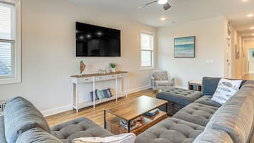 Ein modernes Wohnzimmer mit großem Flachbildfernseher, grauen Sofas, einem Couchtisch und Deckenventilator.