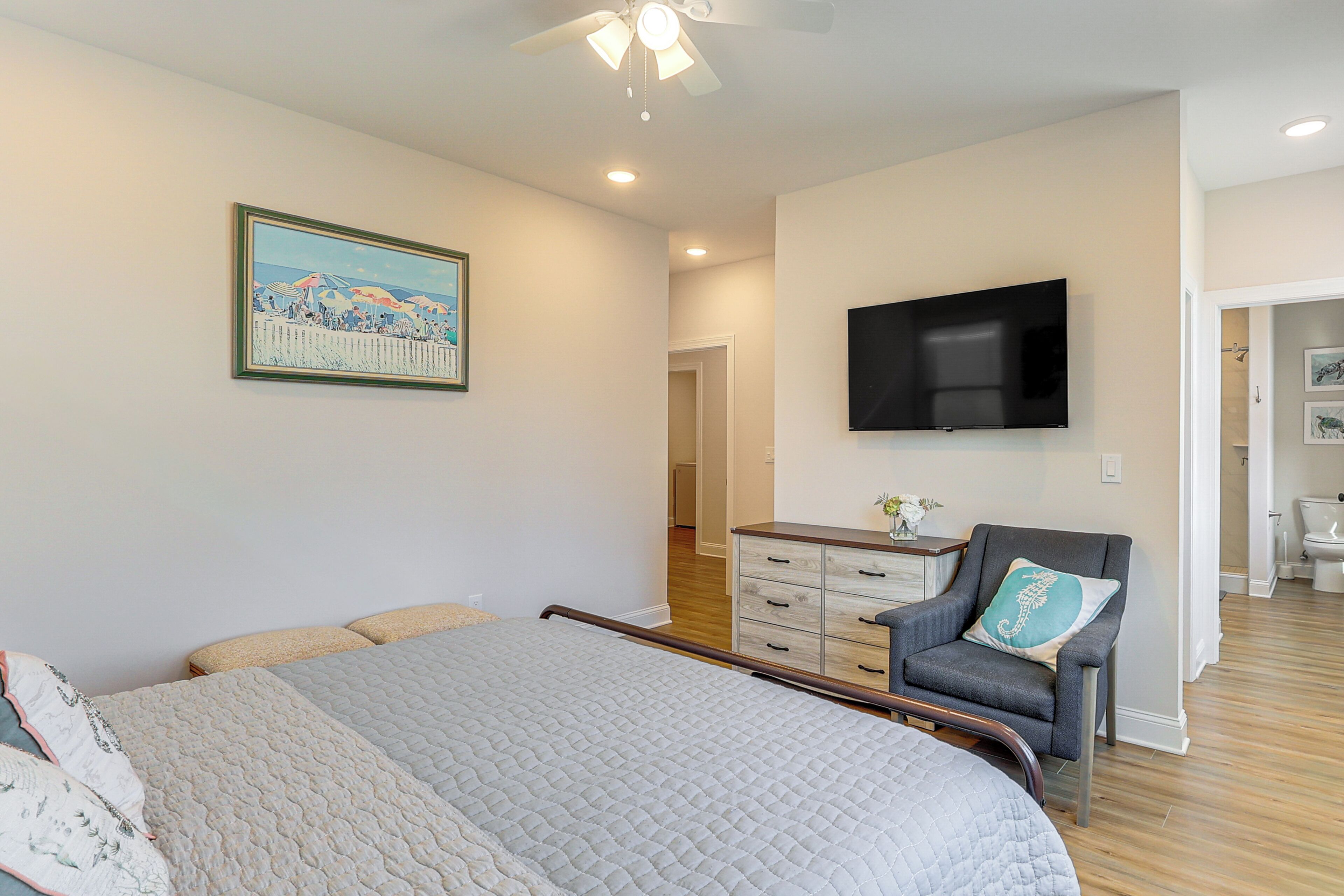 Un dormitorio con cama, una silla, un televisor y un cuadro en la pared.