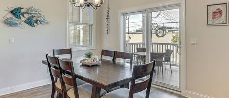A dining area with a wooden table and chairs, a chandelier, and a view of the outdoors through a sliding glass door.