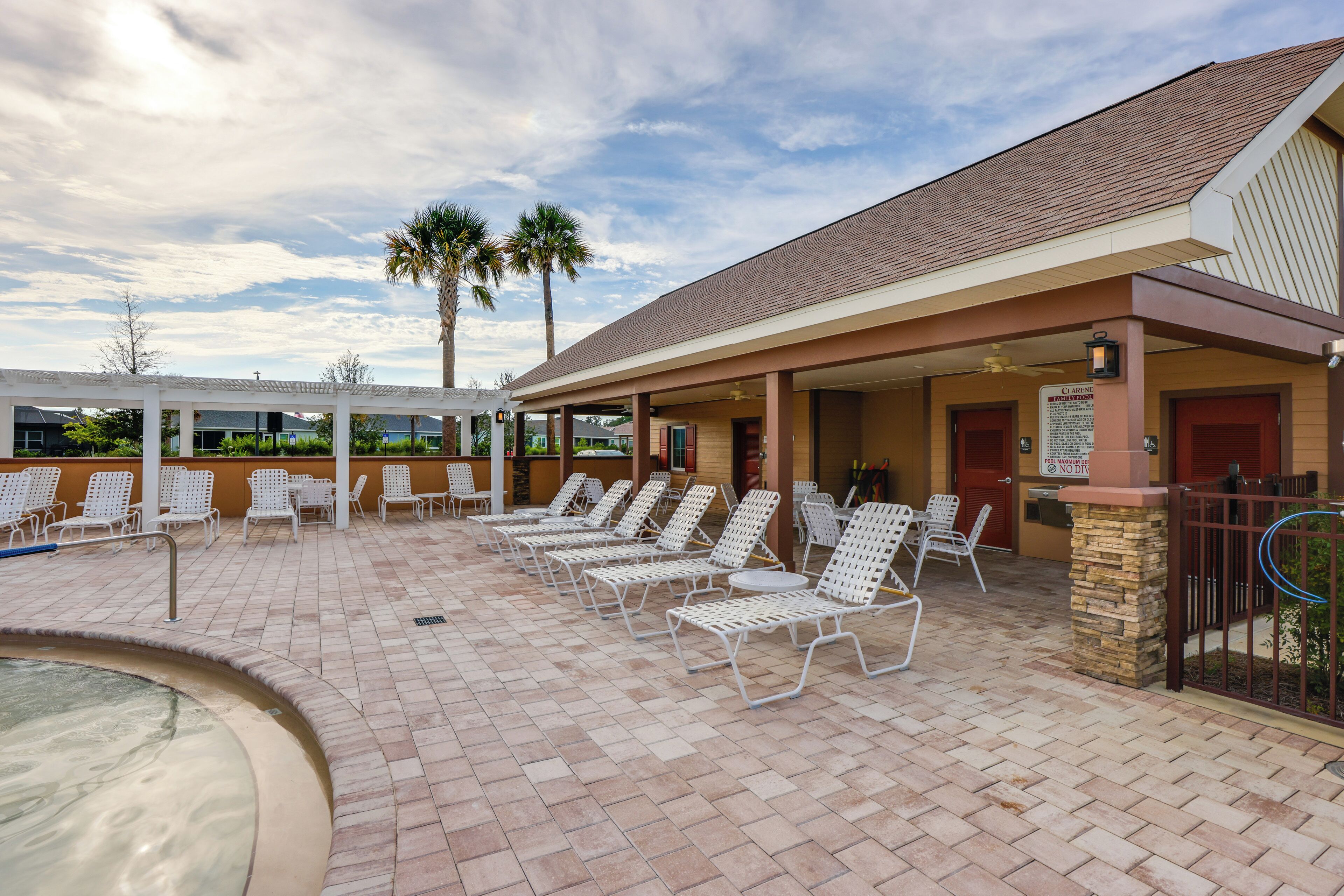 A covered outdoor pool area with lounge chairs and a hot tub.