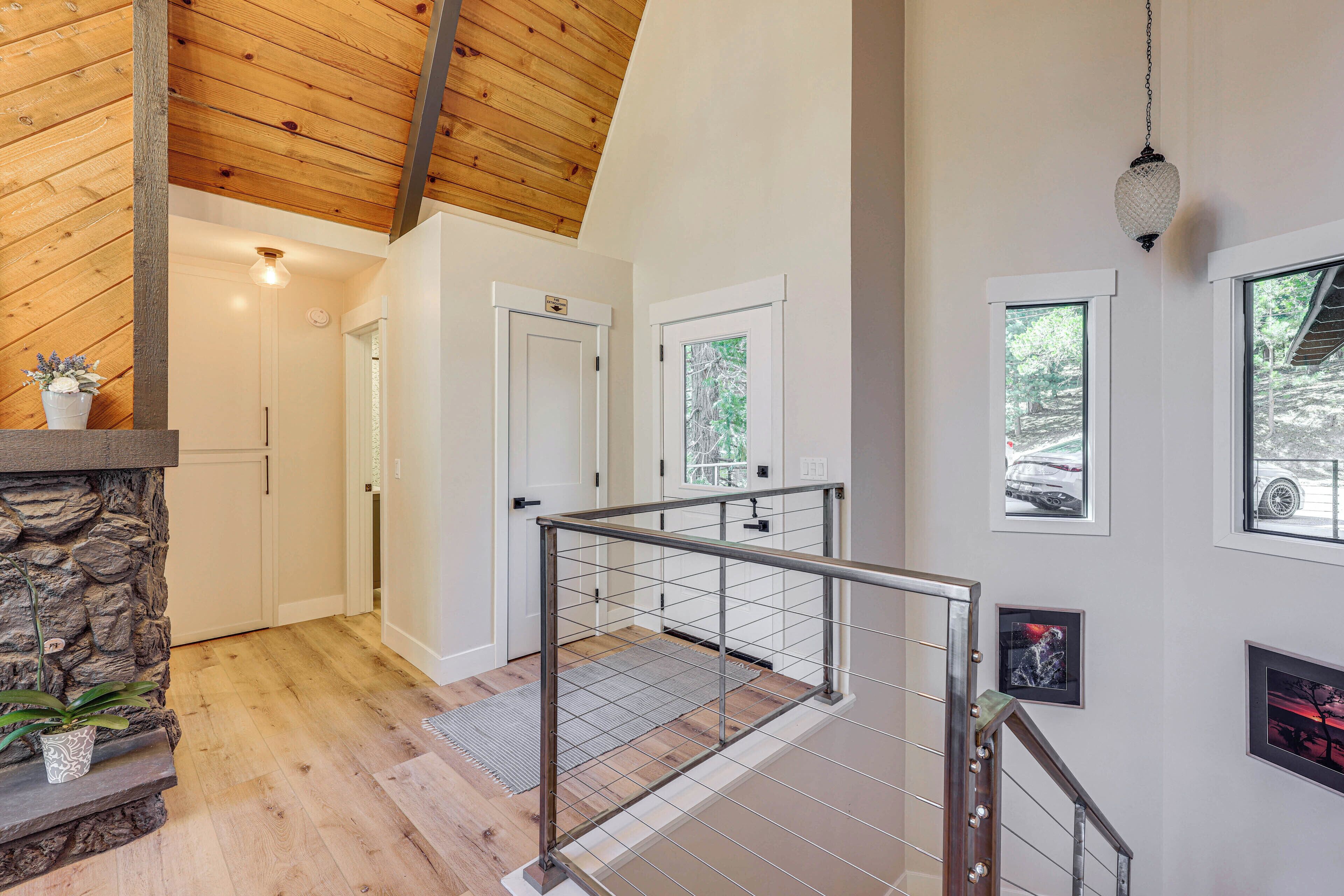 Un intérieur moderne avec un plafond en bois, un mur d’accent en pierre, un escalier avec des rampes en métal et une cheminée.