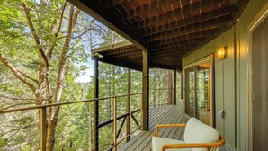 Eine Holzterrasse mit einem Stuhl, umgeben von Bäumen und einem Metallgeländer.