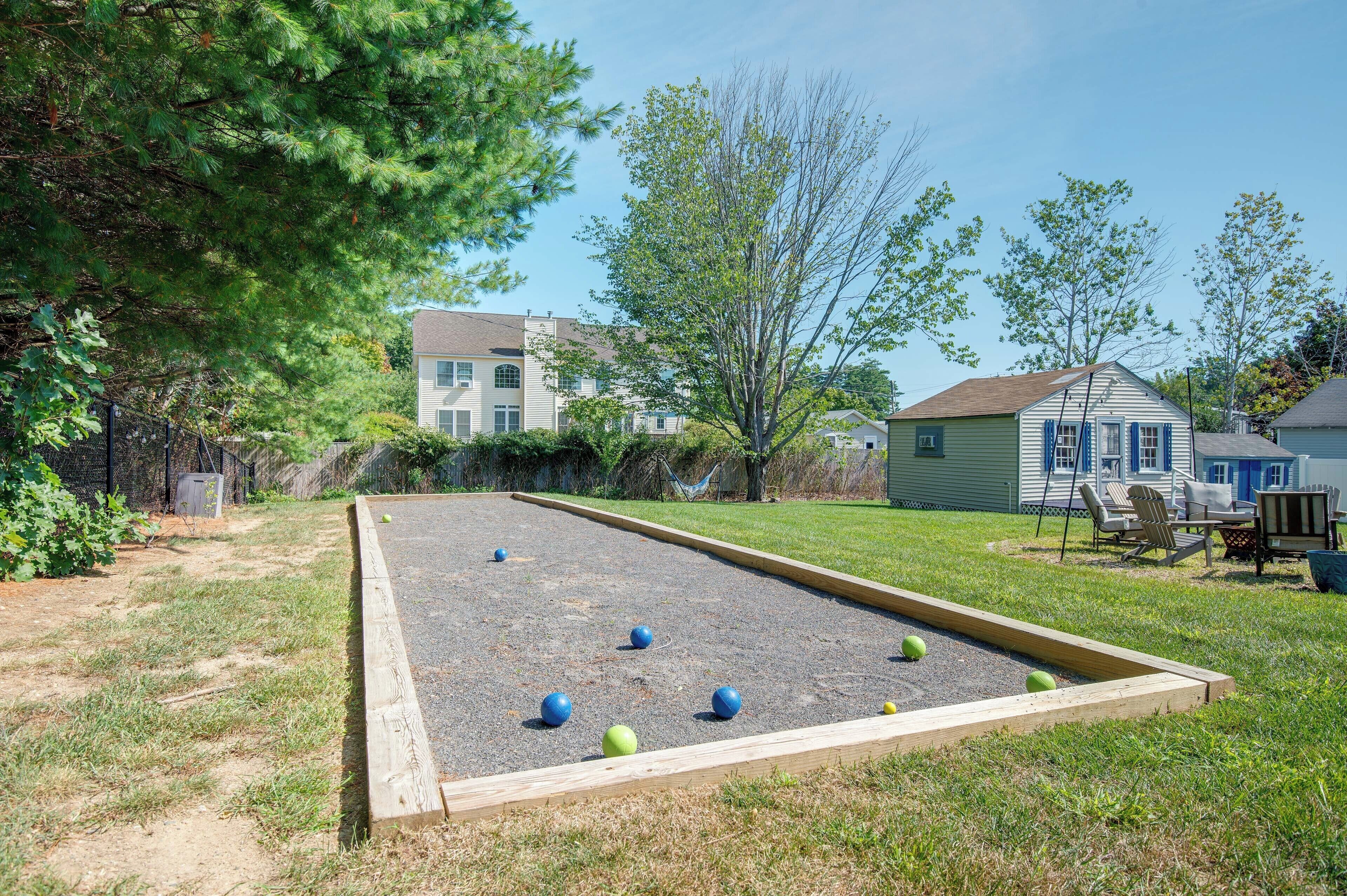 A croquet field with a wooden border, surrounded by grass and trees, with houses in the background.