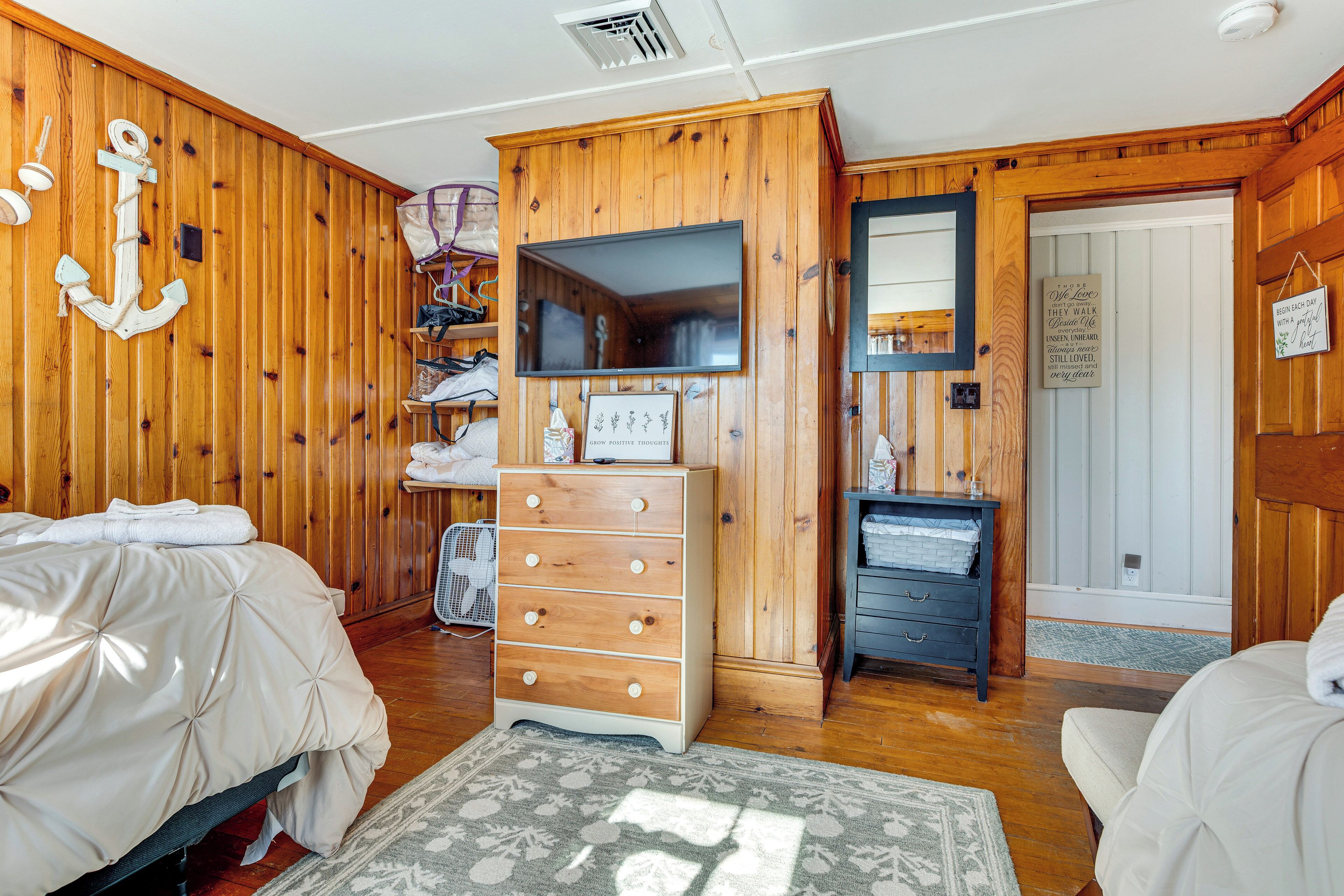 A bedroom with wooden walls, a bed, a dresser, a mirror, and a television.
