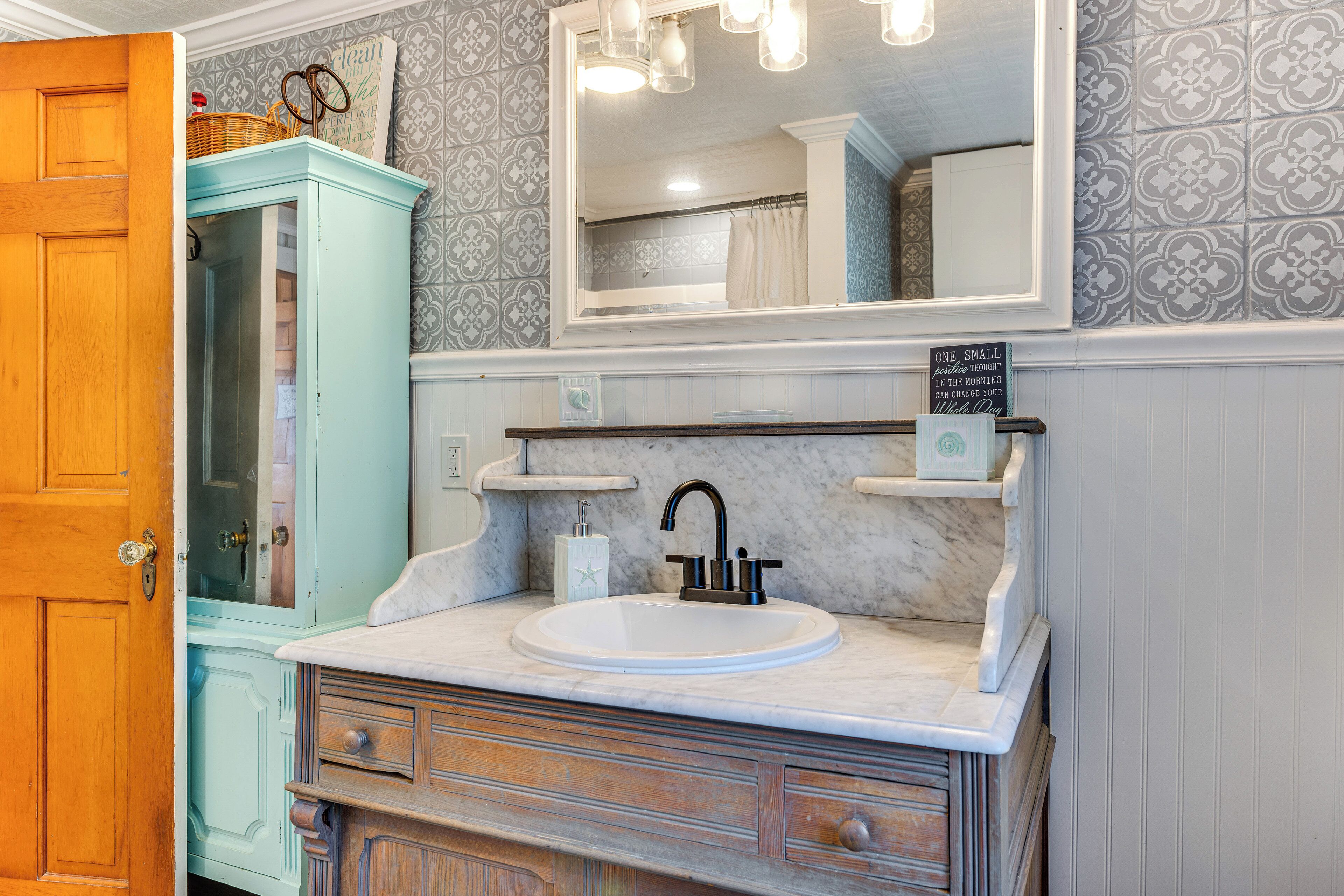 A bathroom with a wooden door, a light blue cabinet, a white sink with a black faucet, and a mirror above the sink.