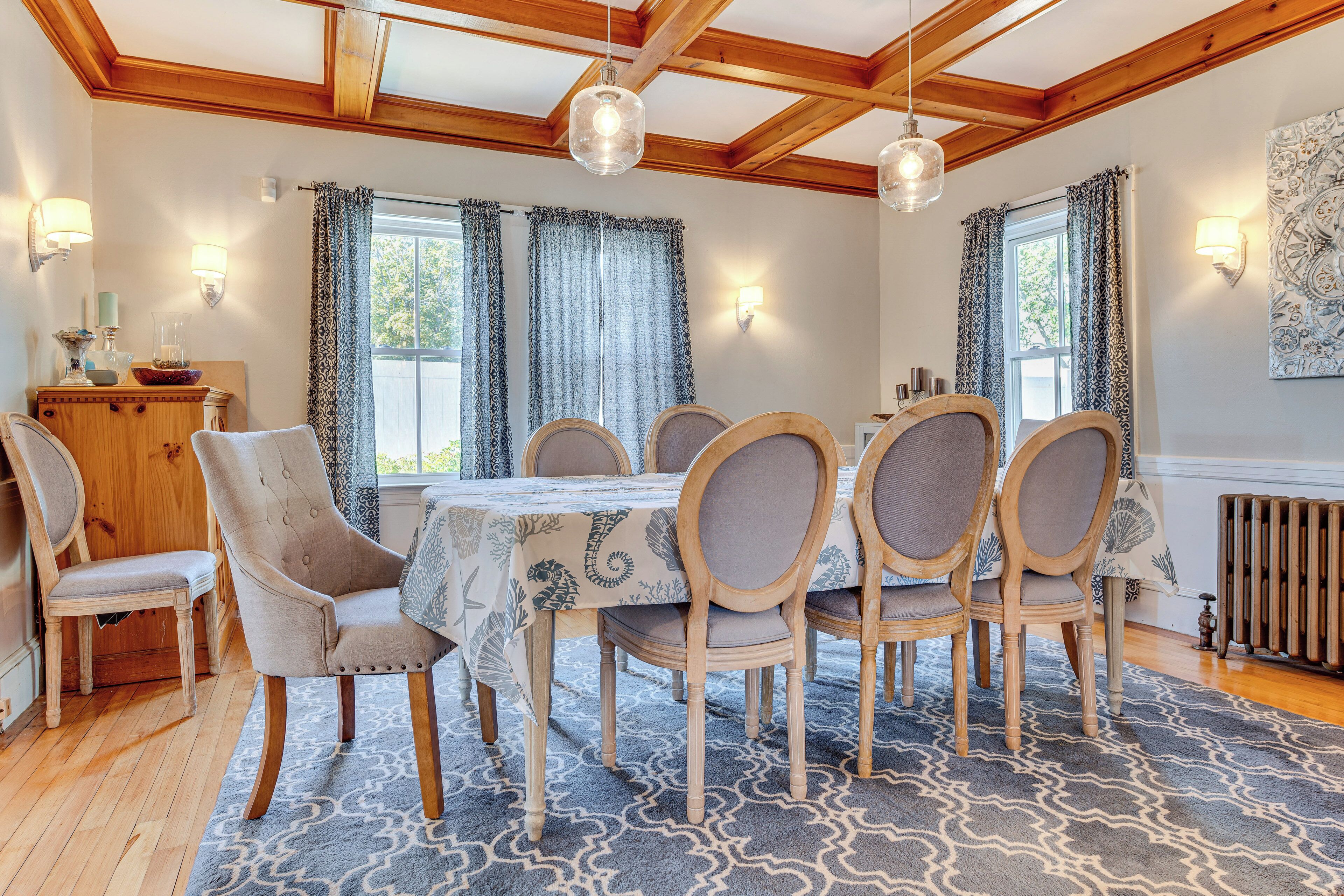 A dining area with a wooden table, six chairs, a patterned rug, and a wooden cabinet.
