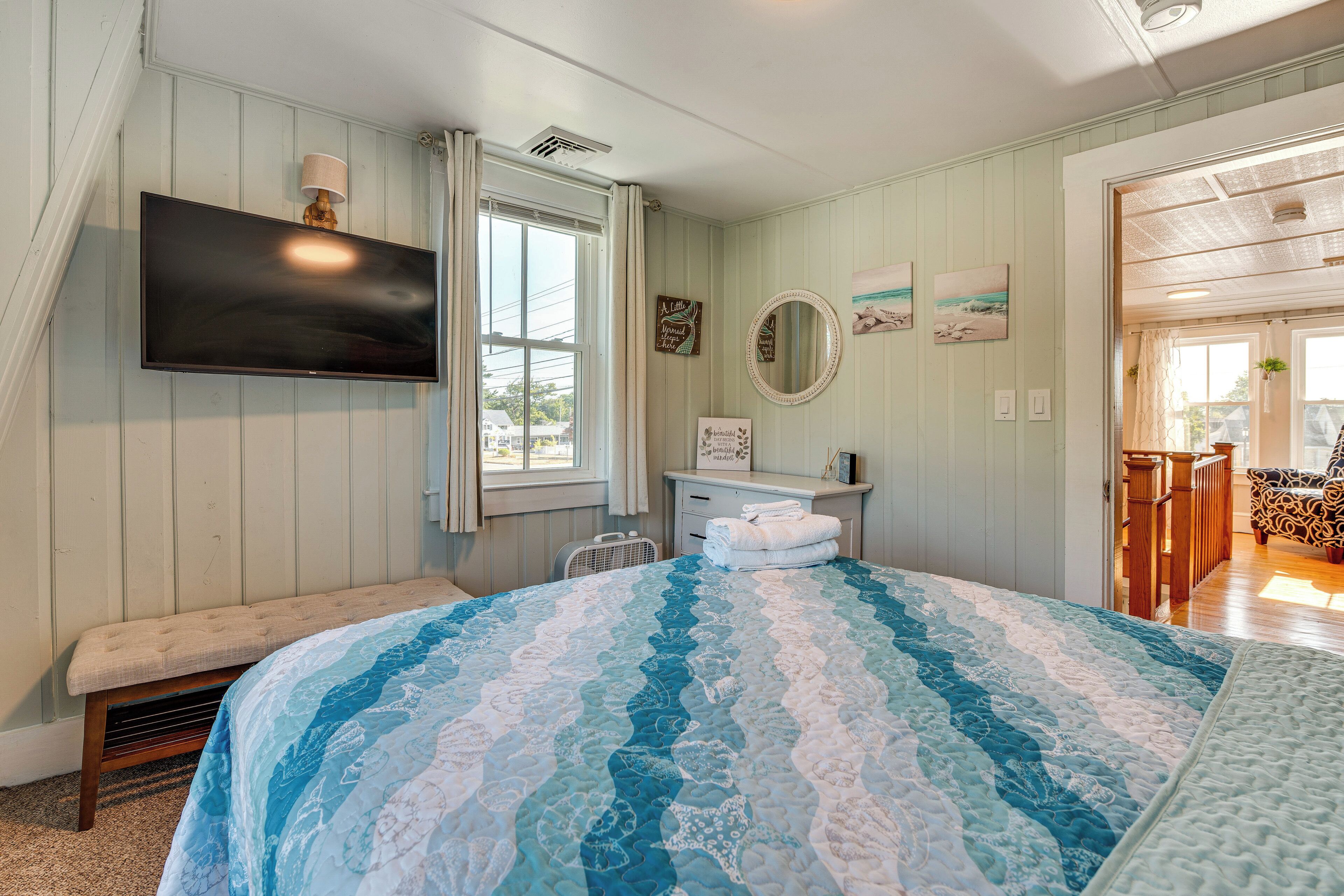 Une chambre à coucher avec un grand lit, un téléviseur à écran plat, un banc, une commode et une fenêtre avec des rideaux.