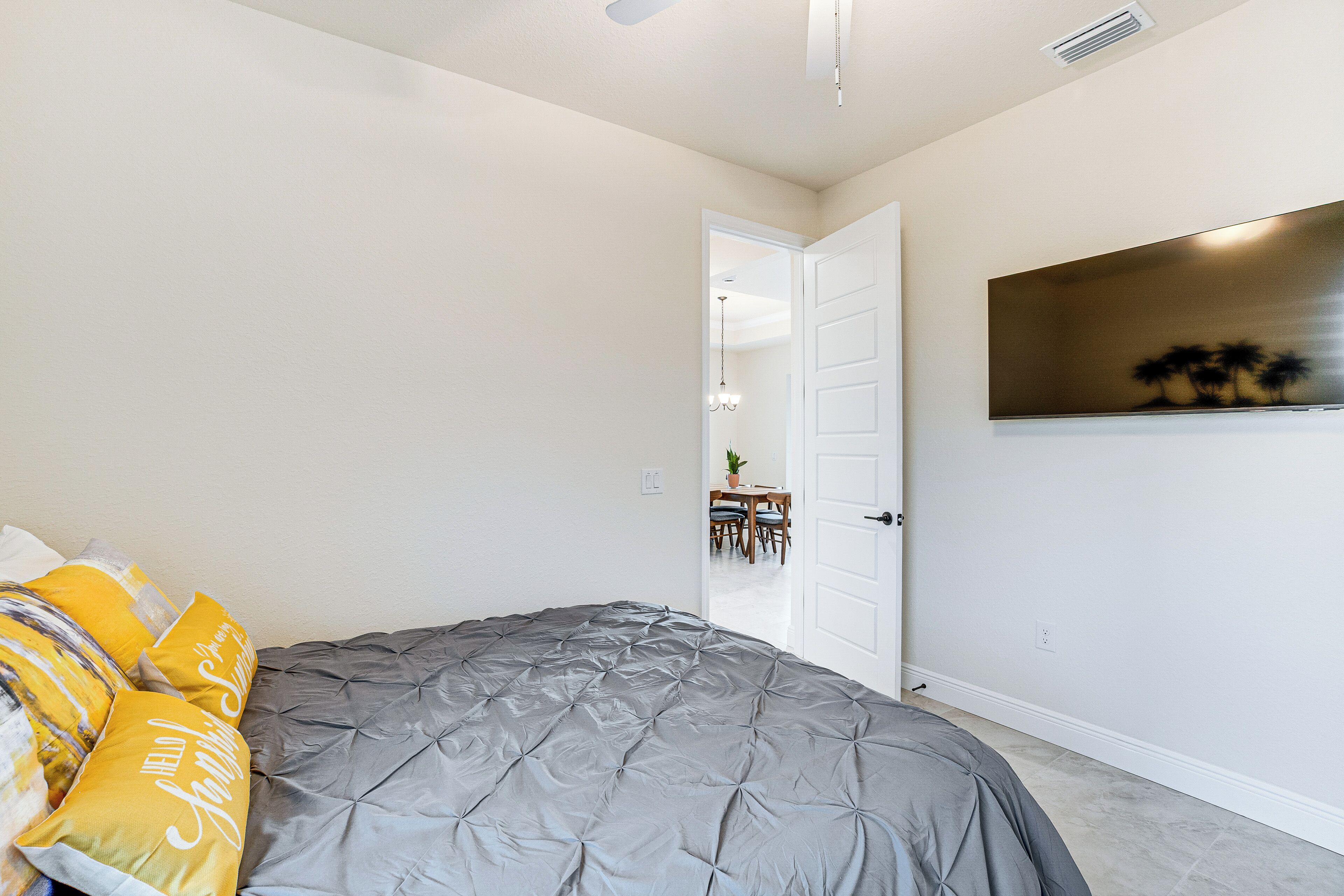 A bedroom with a bed, a door leading to a dining area, and a wall-mounted TV.