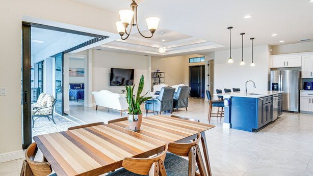 Eine moderne Küche mit einer blauen Kochinsel, ein Essbereich mit einem gestreiften Holztisch und ein Wohnzimmer mit einem großen Fernseher und Sitzgelegenheiten.