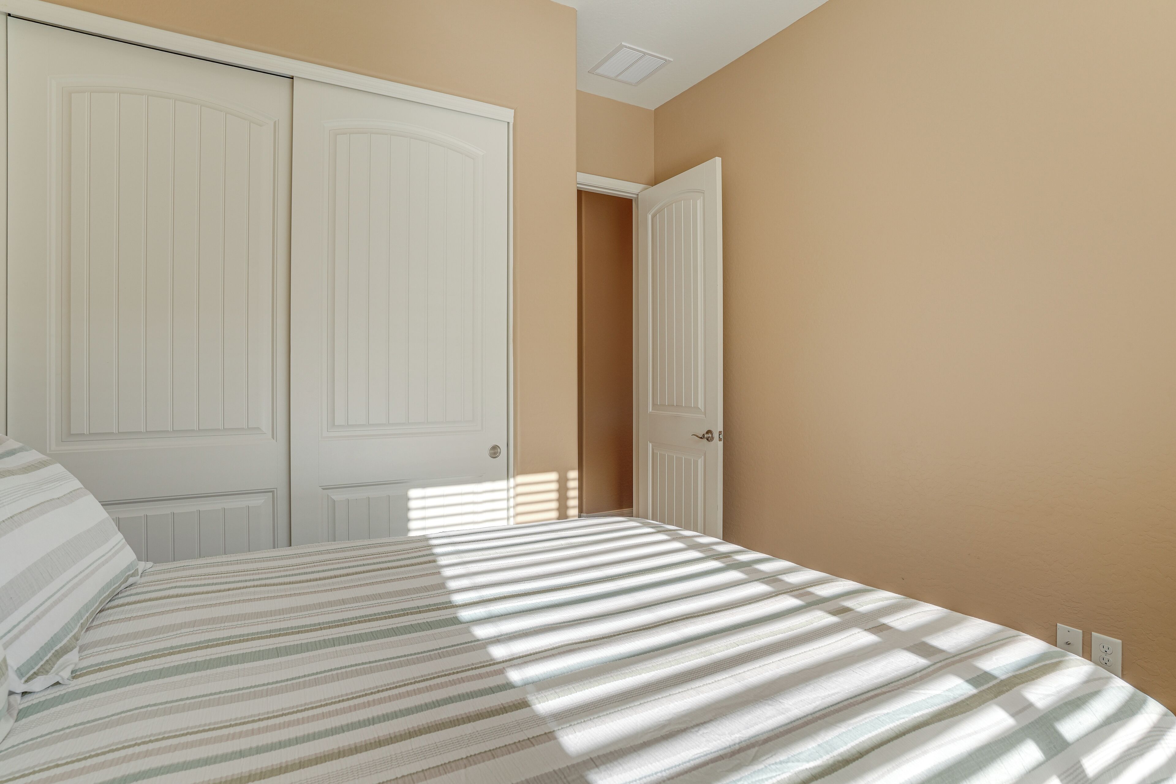Un dormitorio con una cama, dos puertas blancas y una pared color beige.