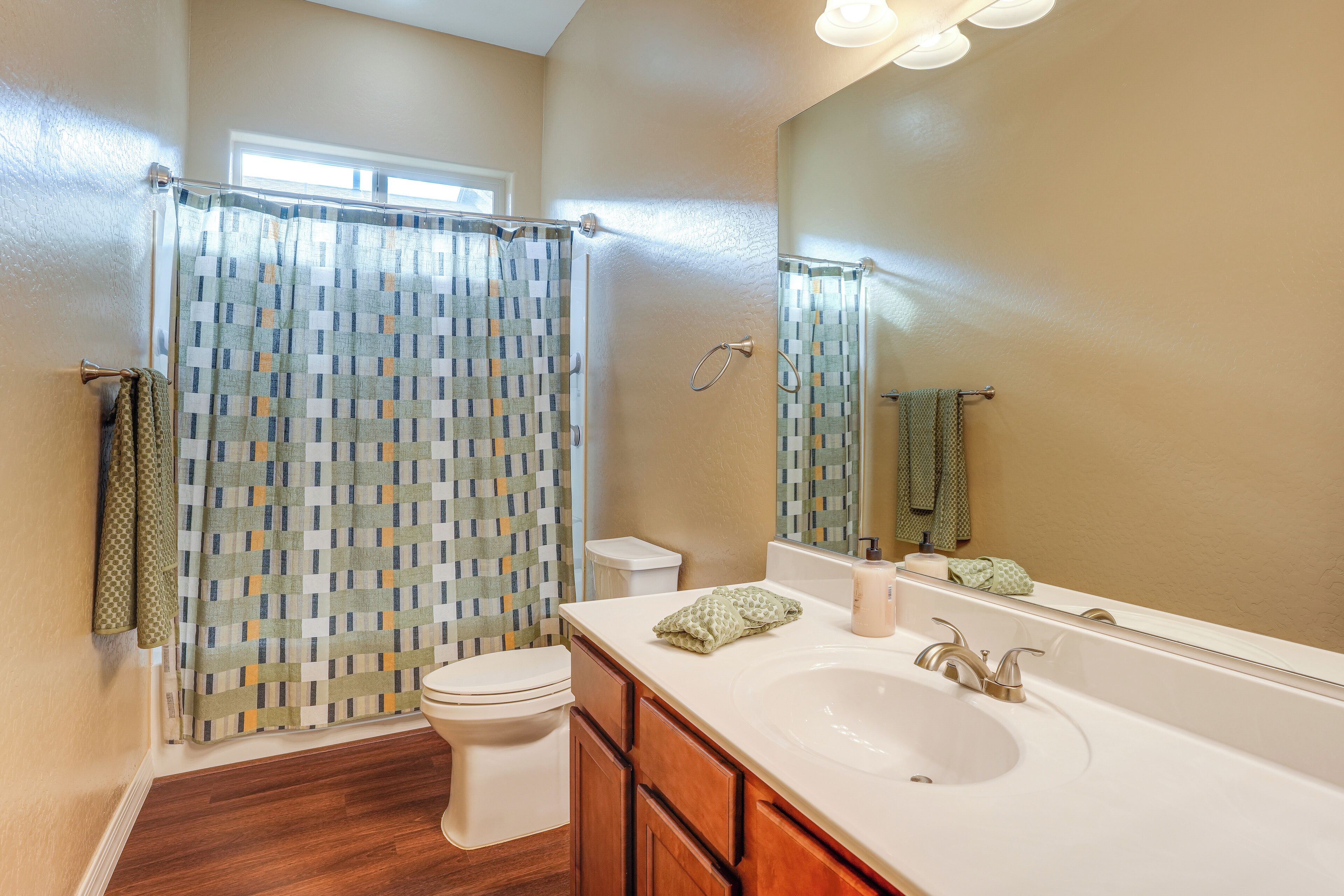 Une salle de bain avec un plancher en bois, un lavabo blanc, un miroir et un rideau de douche à motifs géométriques.