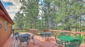 Une terrasse en bois, dotée de mobilier d’extérieur et offrant une vue sur une forêt.