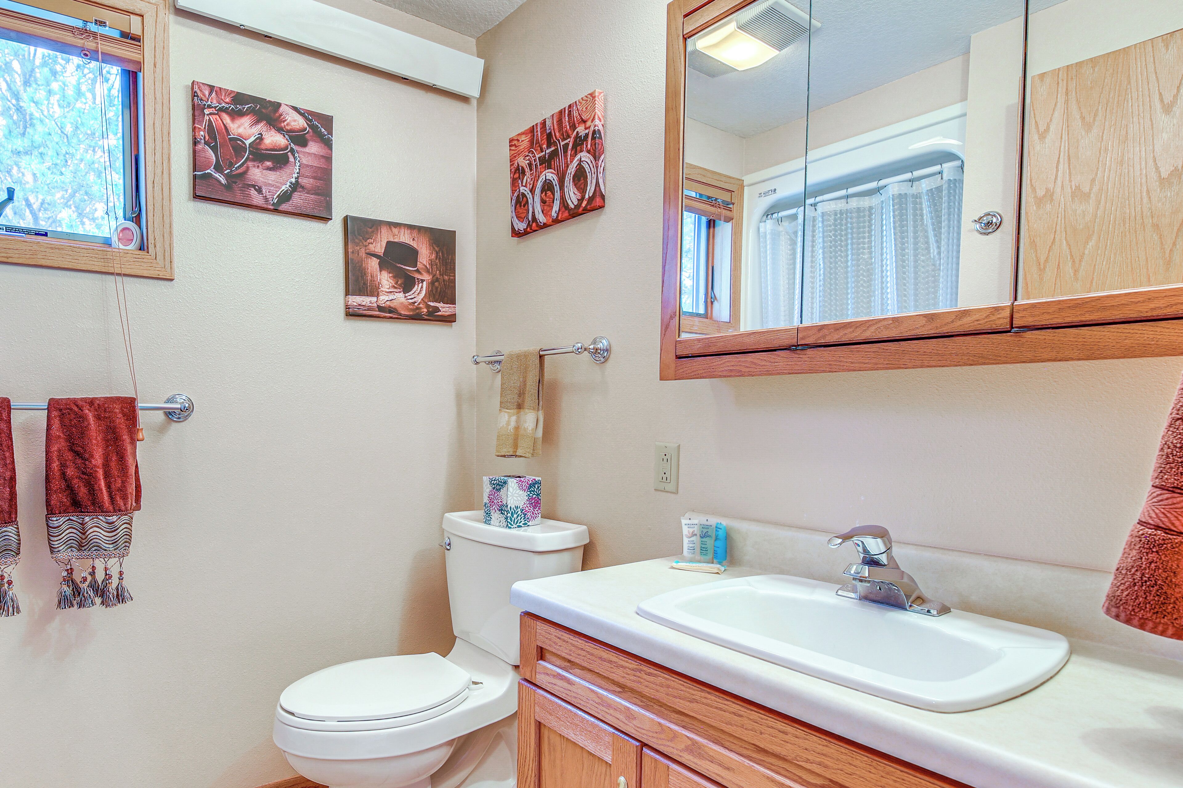 A bathroom with a toilet, sink, and mirror. There are towels hanging on the wall and a picture frame.