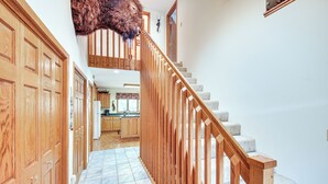 Un escalier en bois avec une rampe menant à un deuxième étage, un coin cuisine avec des meubles en bois et un tapis sur le sol.