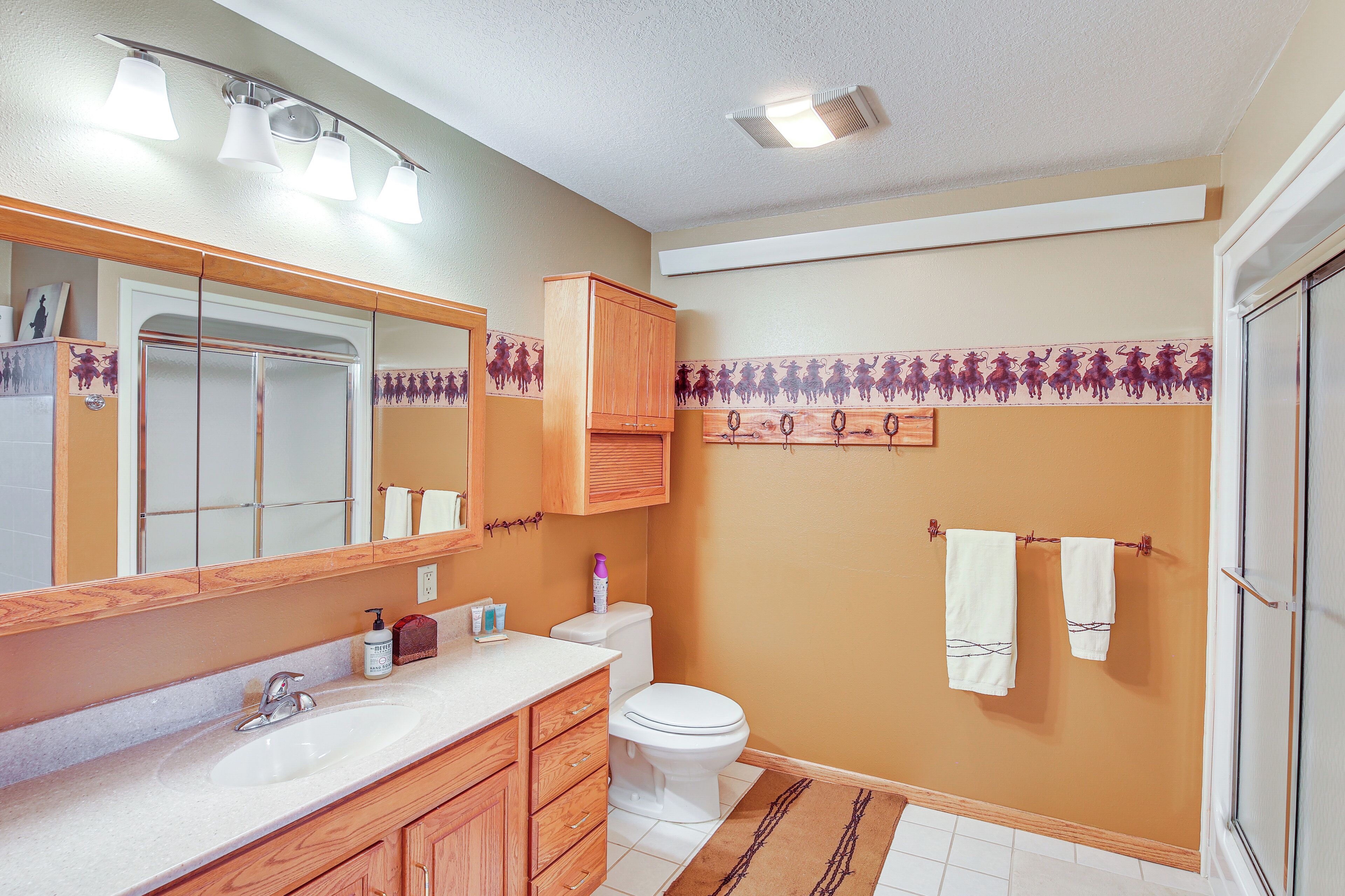 Ein Badezimmer mit einem weißen Waschbecken, Holzschränken, einer Toilette und einem Spiegel.